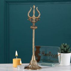 a golden candle holder on a table next to some candles and a potted plant