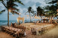 tables set up on the beach for an outdoor dinner party with lights strung from palm trees