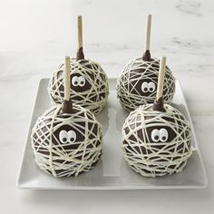 four chocolate covered apples with googly eyes and sticks sticking out of them on a white plate