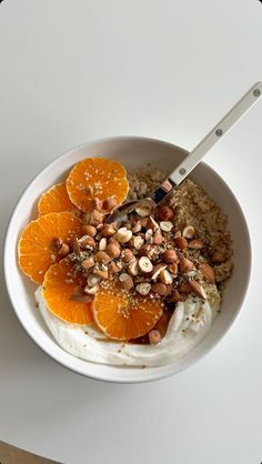 a bowl filled with oatmeal topped with orange slices and nuts next to a spoon