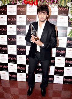 a man standing in front of a wall with flowers holding an award for best performance