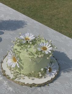 a green cake with white daisies on it sitting on a table in the grass