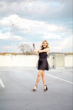 a woman in a black dress is holding a red umbrella and confetti falling from the sky