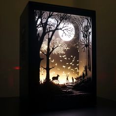 an illuminated box with silhouettes of people and animals in the woods