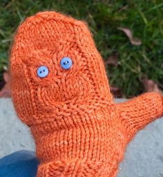 an orange knitted toy with blue eyes sitting on top of a person's lap