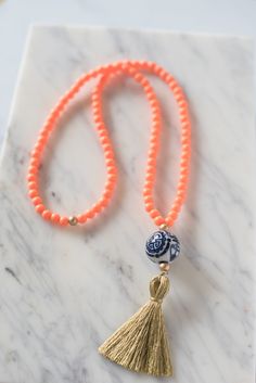 A ginger jar-inspired porcelain bead is accented by orange resin beads and a white tassel. Tassel measures 3.5" and necklace measures 32" long. Handmade in Charleston, South Carolina. Orange Resin, Hand Painted Beads, White Tassel, Tassel Jewelry, Ginger Jar, Charleston South Carolina, Sans Souci, Resin Beads, Beaded Tassels