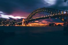 the sydney harbour bridge is lit up at night with lights on it and buildings in the background