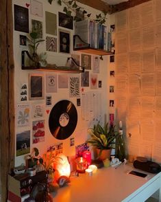 a white desk topped with lots of books and plants next to a wall covered in pictures