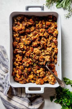 a casserole dish filled with stuffing and topped with parsley on the side