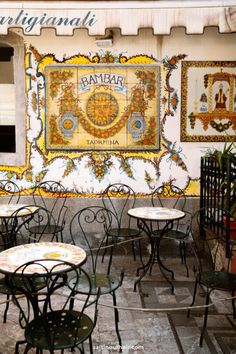 tables and chairs in front of a wall with an ornate painting on it's side