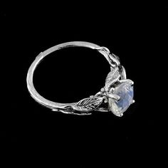 a white gold ring with a blue stone in the center and leaves around it on a black background