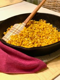 a skillet filled with corn sitting on top of a table next to a pink towel