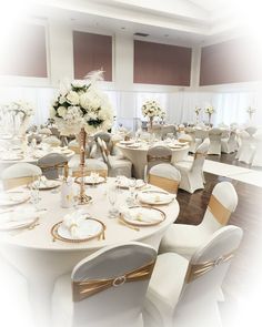 a room filled with tables and chairs covered in white linens, gold trimmings and flowers