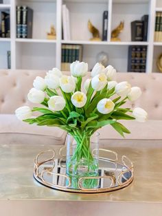 a glass vase filled with white tulips sitting on top of a metal tray