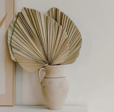 a white vase sitting next to a wall with a fan on it