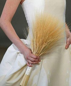 a woman in a white dress holding a bunch of dried wheat on the catwalk