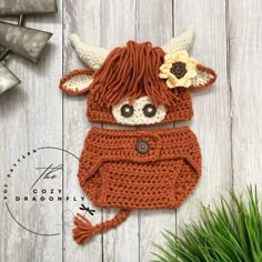 a crocheted cow hat and diaper cover on a white wooden background with grass