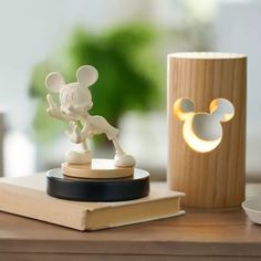 a mickey mouse figurine next to a book on a wooden table with a lamp in the background