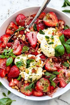 a white bowl filled with strawberries, nuts and spinach on top of a marble counter