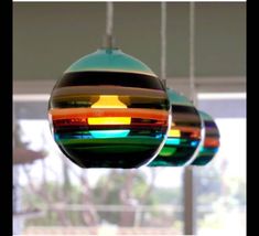 three multicolored glass ornaments hanging from strings in front of a window with blinds