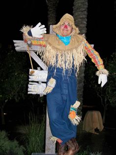 a scarecrow dressed in blue overalls and white gloves standing next to a palm tree