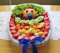 a fruit platter with a teddy bear in the center and blue ribbon around it