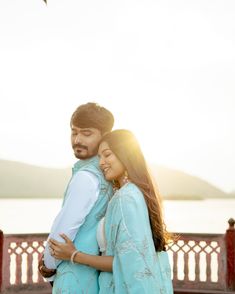 a man and woman standing next to each other in front of a body of water