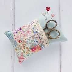 a pair of scissors sitting on top of a pillow with flowers and hearts attached to it