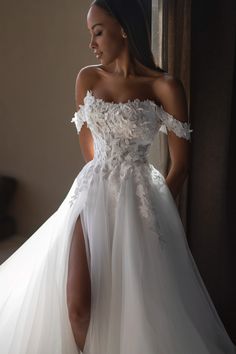 a woman in a white wedding dress standing next to a window with her leg up