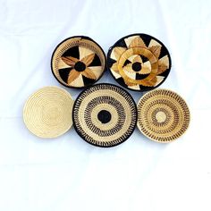 four woven baskets with black and gold designs on the sides, sitting on a white surface