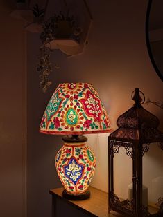 a colorful lamp sitting on top of a wooden table next to a lantern and mirror