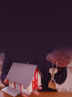 a person holding a house shaped keychain in front of a small model home