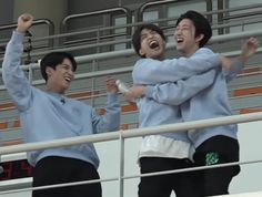 three young men standing next to each other with their arms in the air and laughing