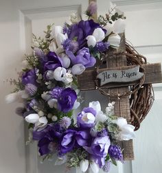 a wreath with purple and white flowers is hanging on the front door, next to a cross