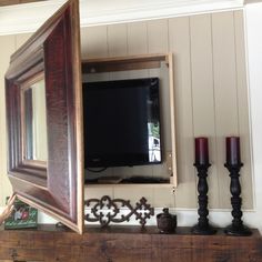 a flat screen tv sitting on top of a wooden shelf next to candles and a mirror