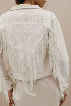 the back of a woman wearing a white jacket with fringes and letters on it