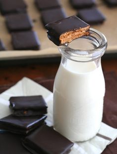 a glass bottle filled with milk and some chocolate pieces on top of it next to a pile of cookies