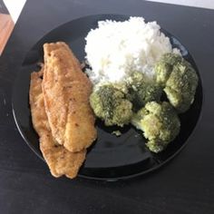 a black plate topped with rice and fish next to broccoli on a table