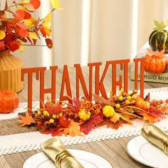 the table is set for thanksgiving dinner with pumpkins, leaves and gold place settings