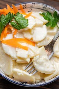 a bowl filled with dumplings, carrots and parsley on top of a wooden table