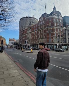 a man standing on the side of a road next to a tall building with lots of windows