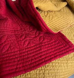 a bed with red and yellow bedspread next to each other on the floor