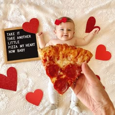 a baby sitting on top of a bed holding a slice of pizza in front of it