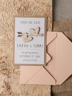 save the date card with two hearts and an arrow on it next to a pink envelope