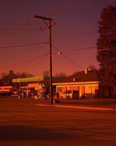 an empty gas station at dusk with no one around it and cars parked on the side of the road