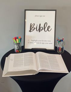 an open bible sitting on top of a table with pencils and markers in front of it