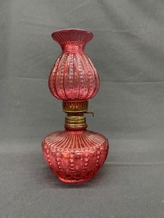 a red glass vase sitting on top of a gray table next to a white wall