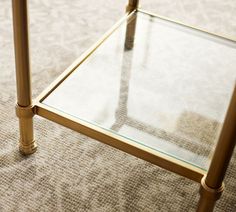 a glass top coffee table with gold legs on carpeted floor next to lampposts