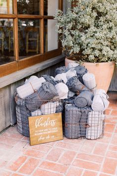 two baskets filled with blankets sitting on top of a brick floor next to a potted plant