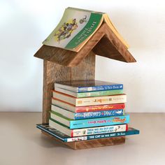 a stack of books sitting on top of a wooden house shaped like a birdhouse